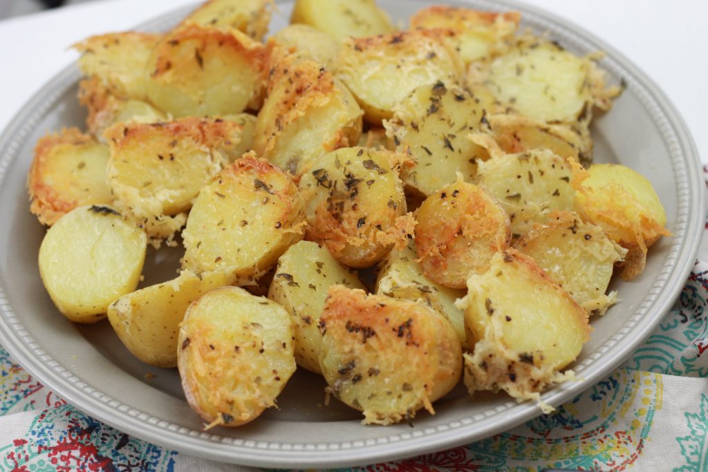 Baked sliced petite yellow potatoes, topped with shredded parmesan cheese served on a plate.