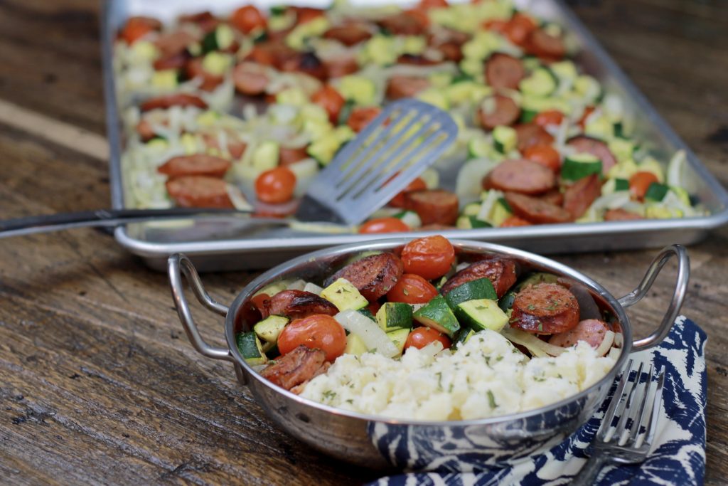 Sausage, zucchini, petite tomatoes, and chopped onions served in a bowl with a side of white rice.