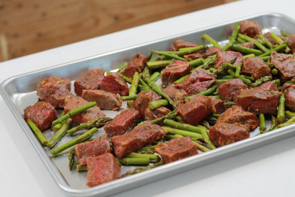 Sheet pan with spicey steak bites and asparagus ready to be broiled on a pan.