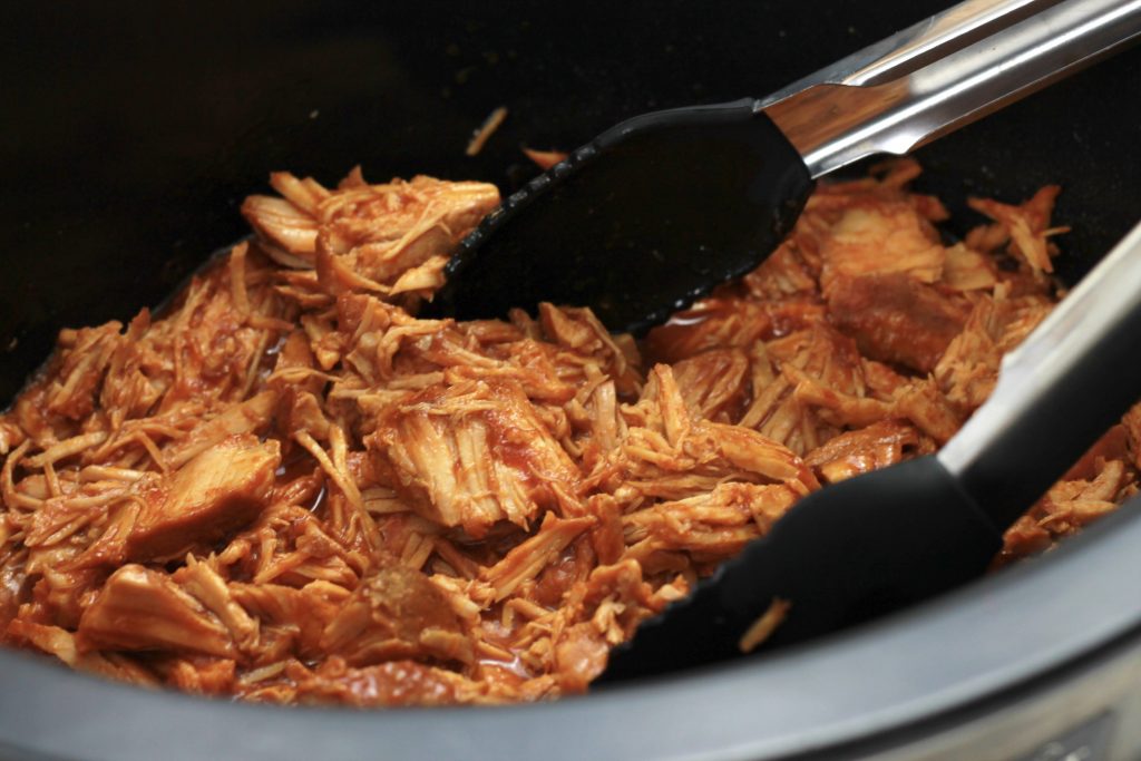 Cooked pork with BBQ sauce and ketchup shredded in a crockpot ready to be served.