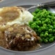 Salisbury steak with brown gravy on a gray plate served with mashed potatoes and green peas