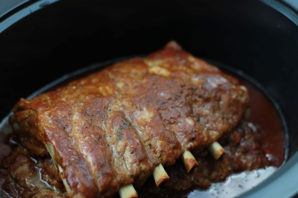 One slab of pork ribs drowned in BBQ sauce and placed in a crock pot to be cooked.