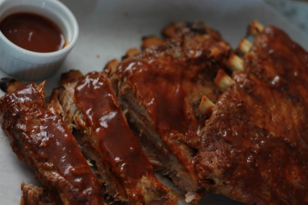 Tender slow cooked pork ribs topped with BBQ sauce and served with a side of extra BBQ sauce.
