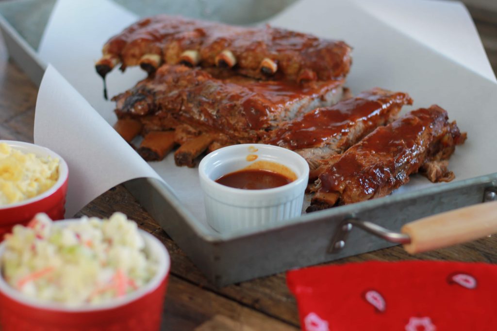 Tender cooked pork lab ribs stacked and served with BBQ sauce on a tray with a side of coleslaw.