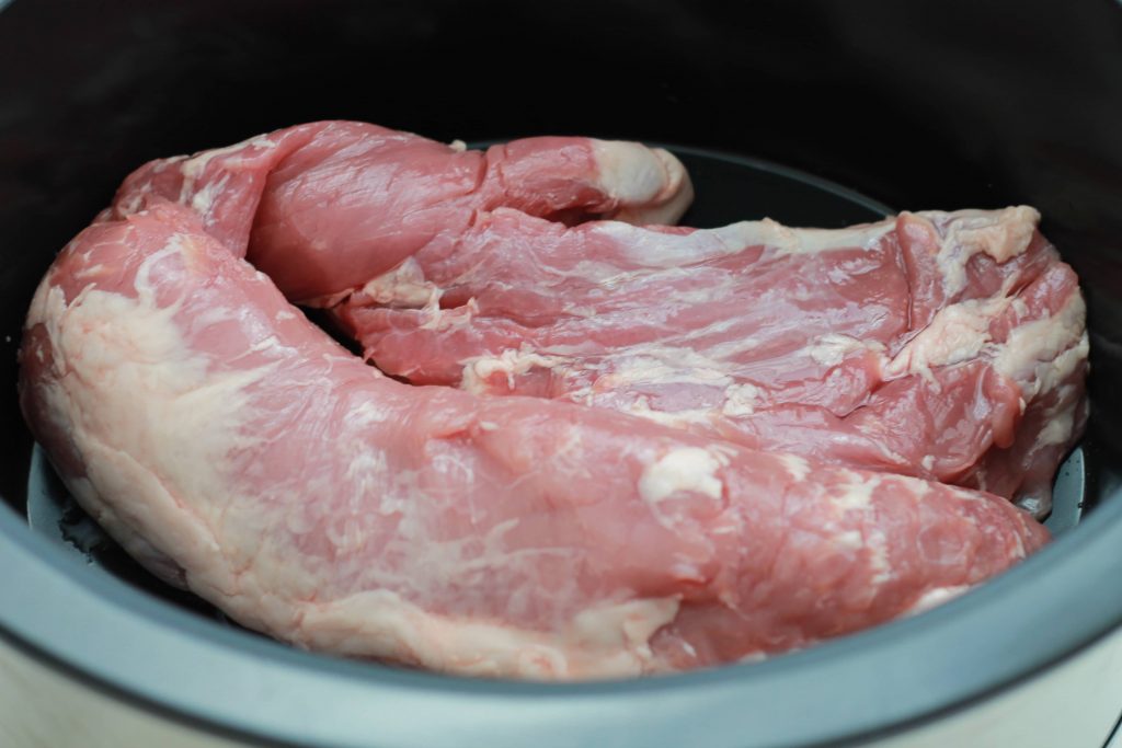 Uncooked piece of pork tenderloin placed in a crockpot ready to be cooked.