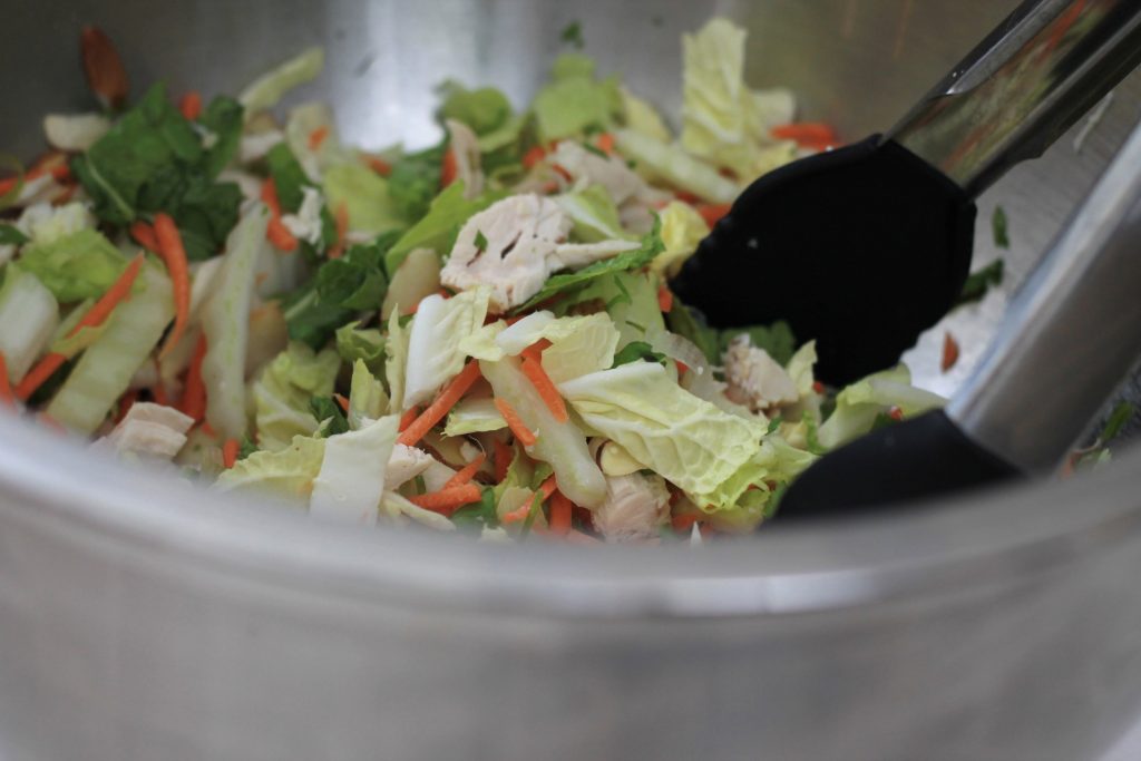 Dry sliced lettuce, mixed with thin carrots, and chicken mixing in a bow.