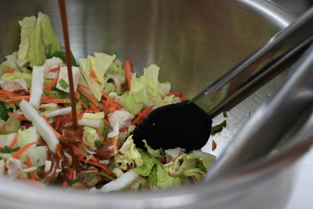 Adding Hoison sauce into a bowl of chopped lettuce and carrots ready to be mixed.