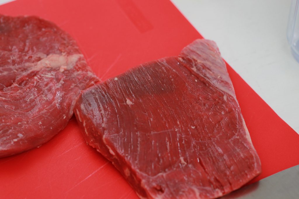 two pieces of uncooked flank steak placed on a red cutting board
