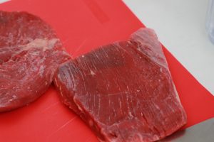 Two cuts of steak on a red colored cutting board.
