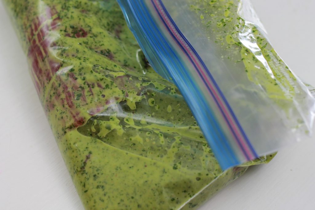 Two pieces of flank steak marinating in seasonings in a clear zip lock bag