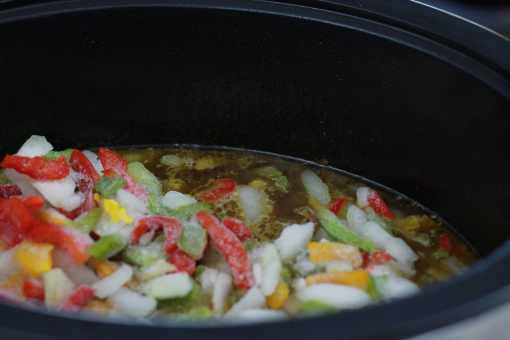 frozen peppers and onions placed in the crockpot accompanied by the marinated flank steak all ready to cook.