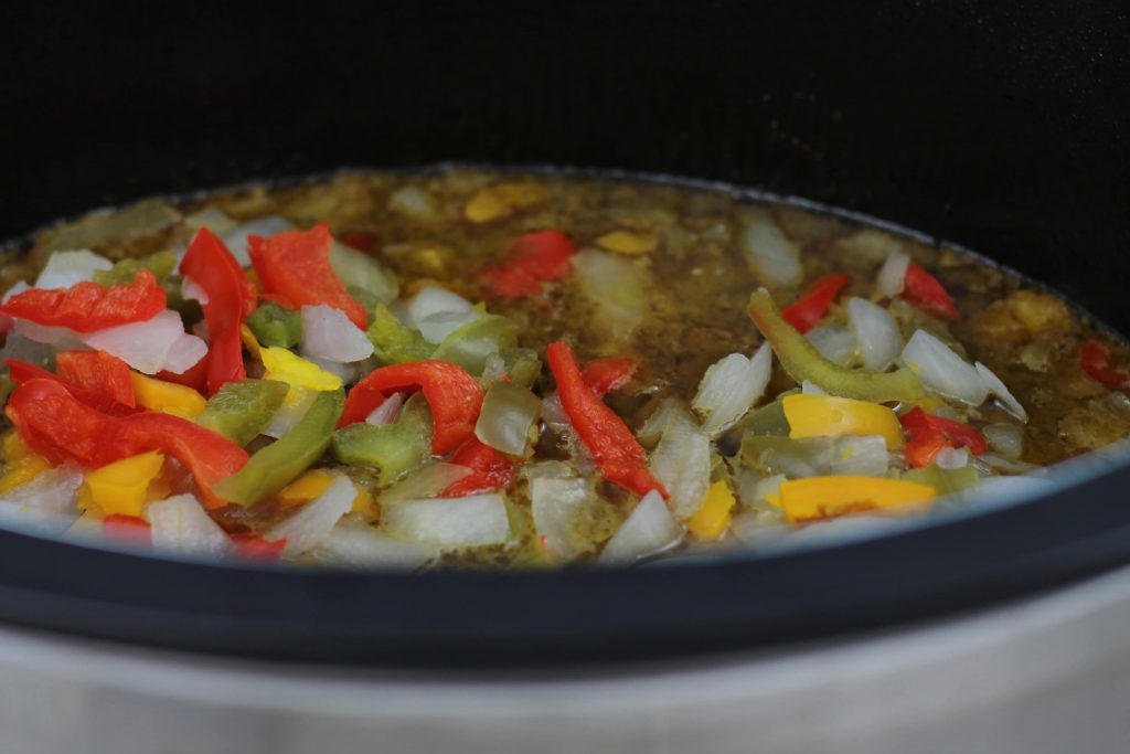 frozen peppers and onions placed in the crockpot accompanied by the marinated flank steak all ready to cook.