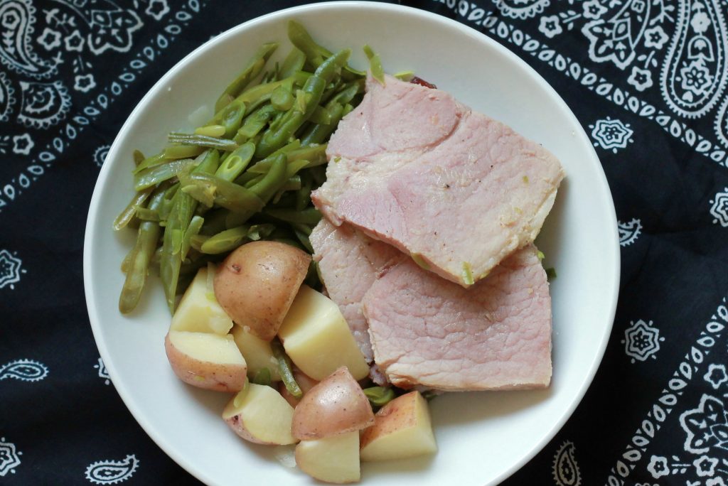 slow cooked ham with cooked green beans served with a side of slow cooked diced potatoes all served on a white plate.
