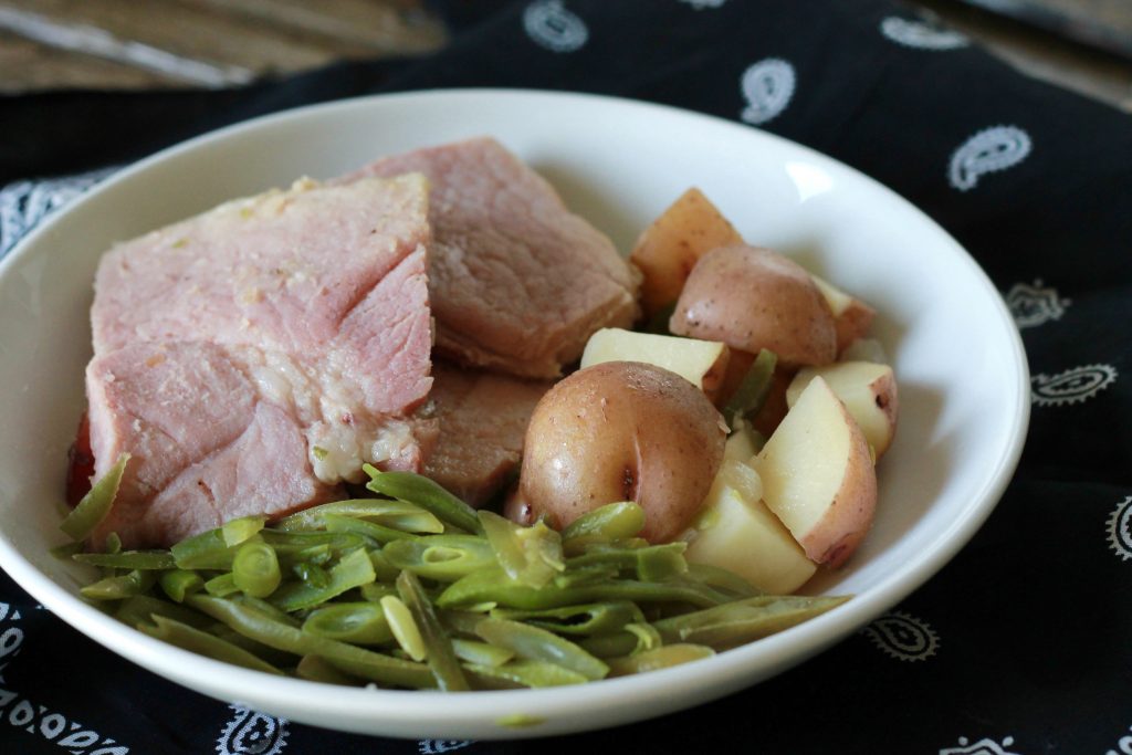 slow cooked ham with cooked green beans served with a side of slow cooked diced potatoes all served on a white plate.