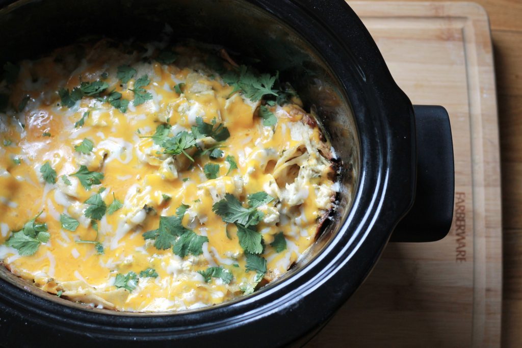 SLOW COOKER SOUR CREAM ENCHILADA CASSEROLE in a black crock pot on a wooden cutting board 