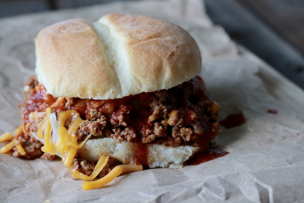Slow cooked ground beef mixed with shredded cheese served on a white hamburger bun.