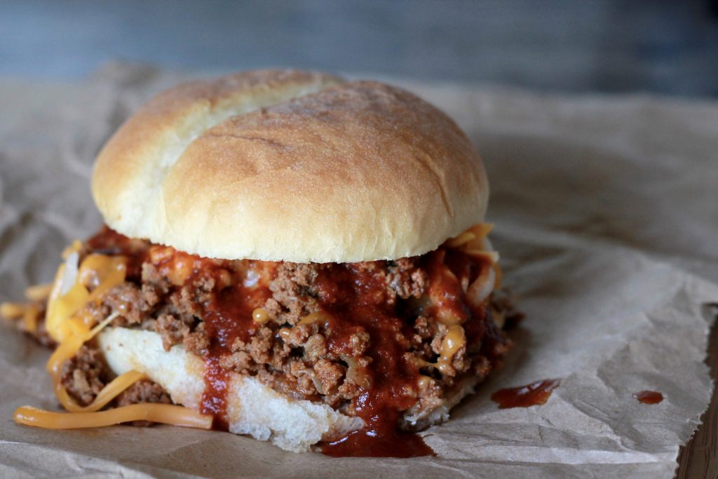Slow cooked ground beef mixed with shredded cheese served on a white hamburger bun.