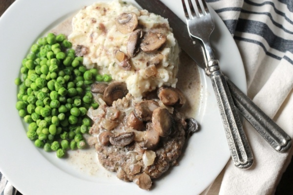 Salsbury Steak with a creamy brown gravy, served with mash potatoes and green peas.