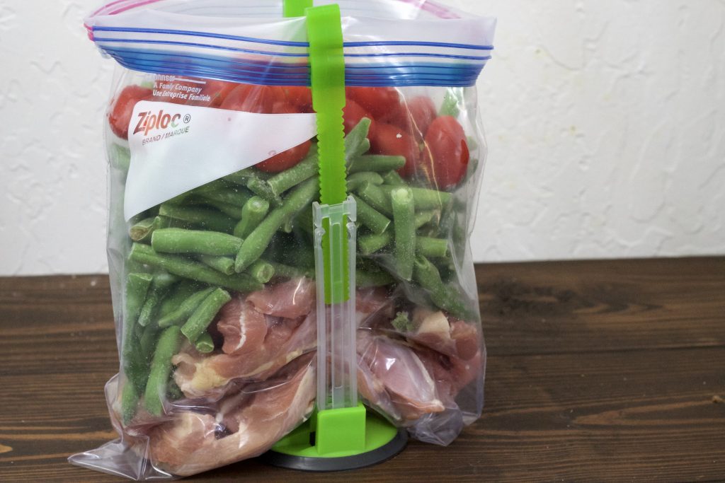 a clear sip lock bag with uncooked chicken, green beans, and petite tomatoes all in a clear bag ready to be shaken