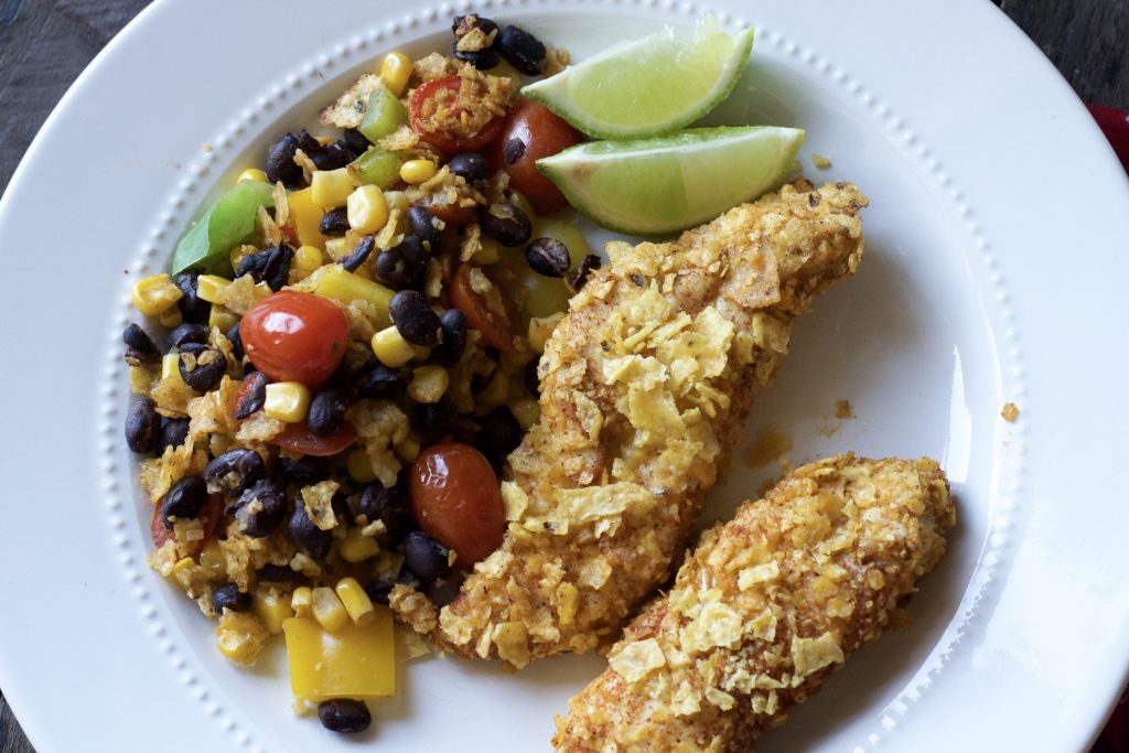 close up view of crispy tortilla chicken strips with black bean and corn warm salad served on white dinner plate.
