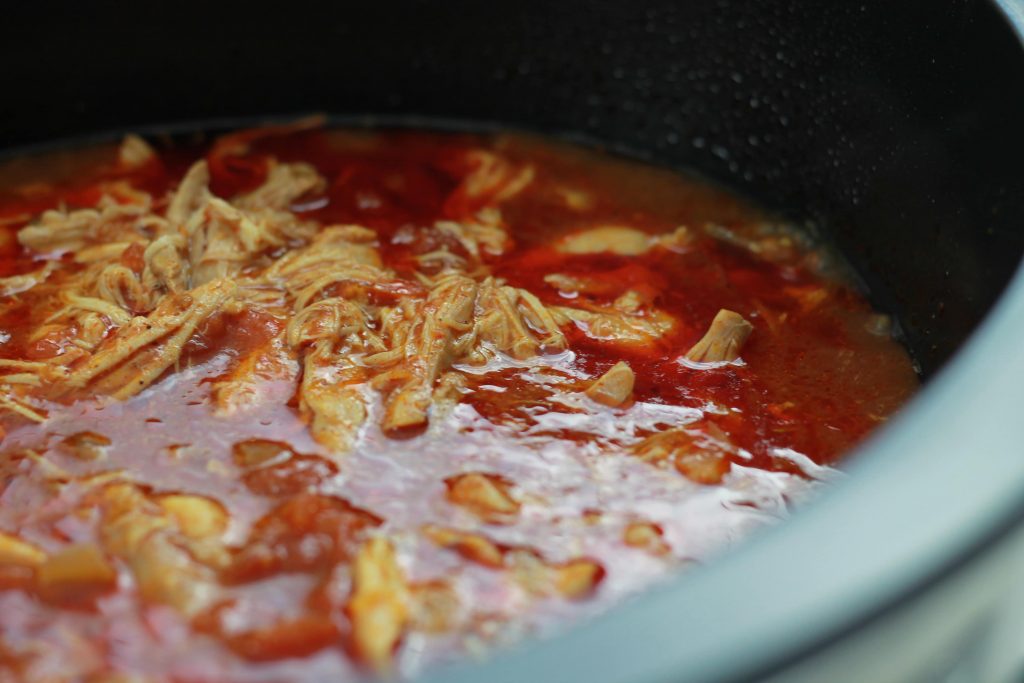 Shredded chicken soaking in taco seasoning in a crock pot ready to be cooked.