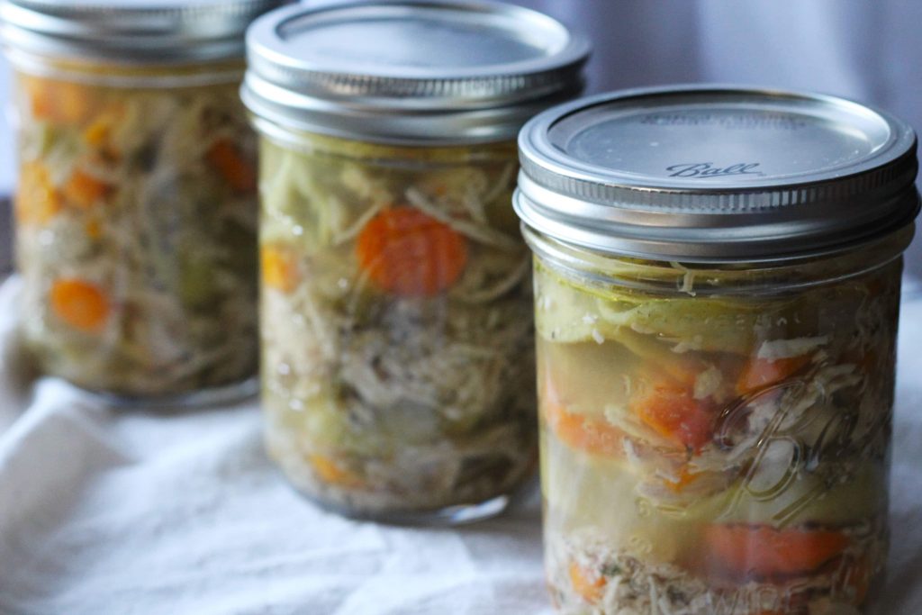green tortellini noodles with slow cooked sliced carrots and shredded chicken in three clear mason jars.