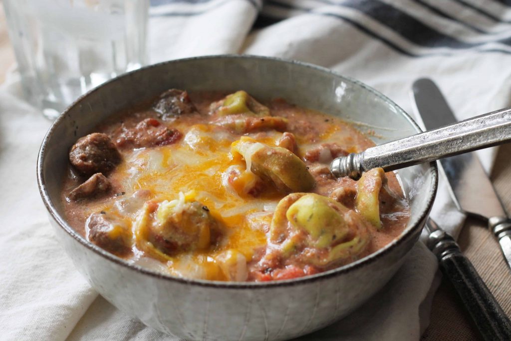 tortellini soup with melted cheese in a tan bowl with spoon and napkin