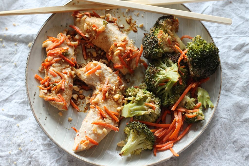 uncooked chicken topped with peanuts on a light blue plate with a side of broccoli and shredded carrots