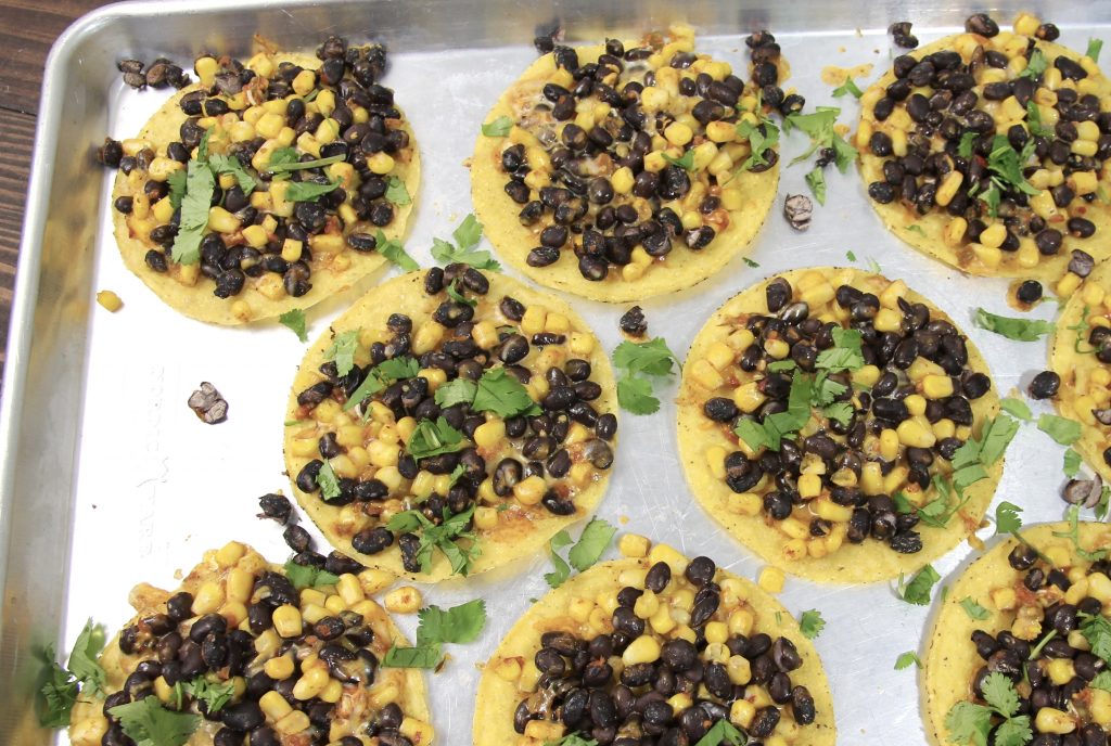 black bean and corn with shredded cheese on crispy tostadas topped with green cilantro on a silver one pan baking sheet.