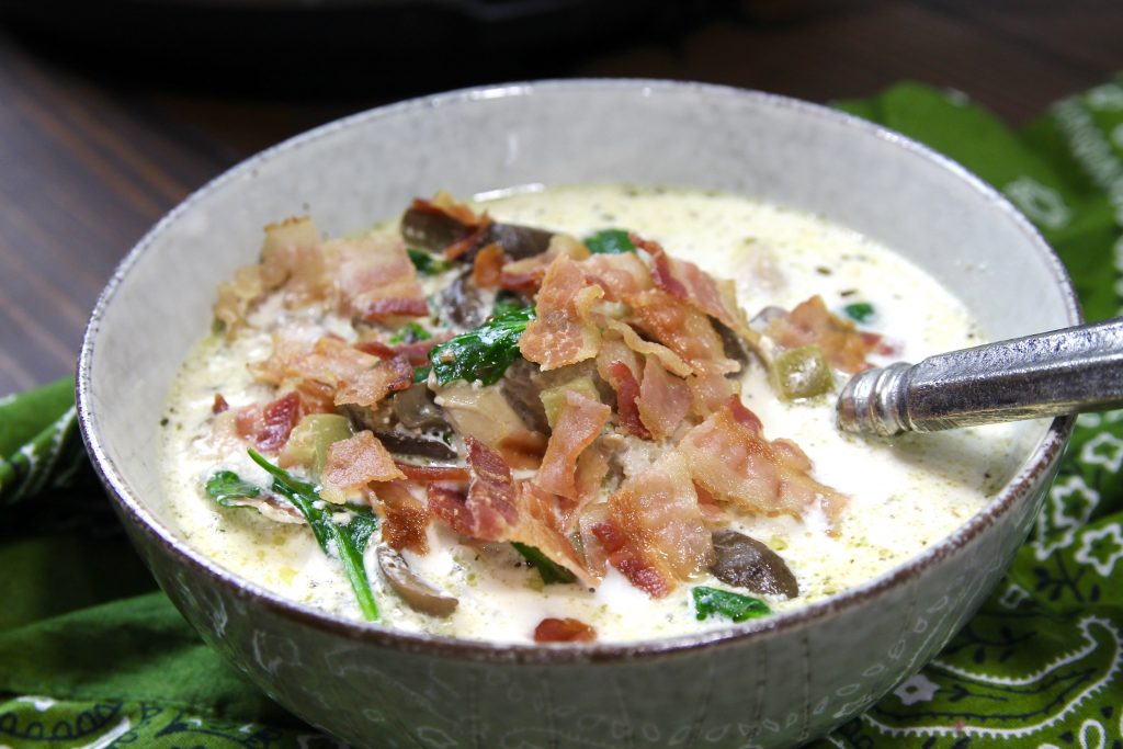 chicken, bacon, mushrooms, spinach, all mixed together win broth with melted butter heavy whipping cream and thyme in a white bowl and silver spoon on top of a green bandana.
