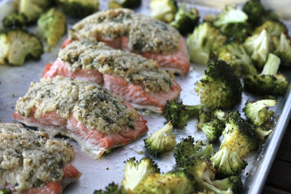 cooked broccoli and salmon topped with mayonnaise, parmesan cheese, almond meal, parsley and lemon, all in one pan silver baking sheet.