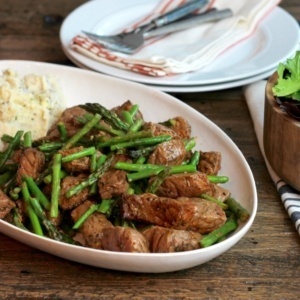 Broiled steak bites with asparagus. Served on a oval dish with mashed potatoes.