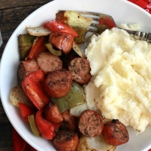 Roasted Sausage, Peppers and Onions on a white plate served with mashed potatoes.