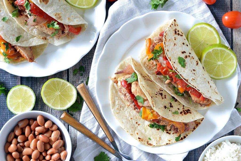 chicken fajitas on white plate with pinto beans, limes and rice