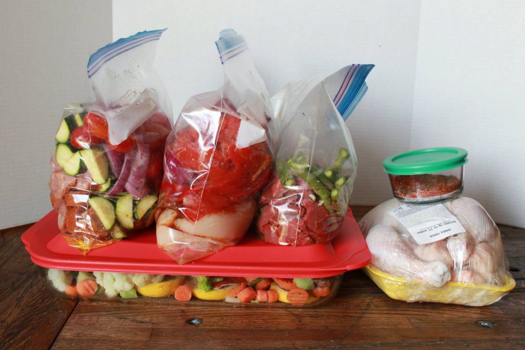 Three clear plastic bags meal prepped and to to cook sitting on top of another meal ready to be cooked along side of an cooked chicken all ready for the week.