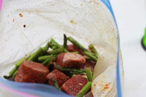 Chopped seasoned steak with green beans, seasoned and mixed in a clear plastic bag.