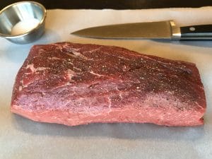 Seasoned beef on parchment paper with a small dish of salt next to a knife.