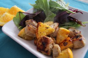 Broiled chopped pork, with orange slices and lettuce served on a plate.