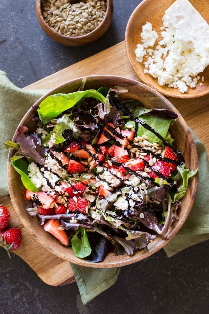 Spinach and greens salad topped with chopped strawberries,nuts and feta cheese with balsamic vinegar in a bowl.