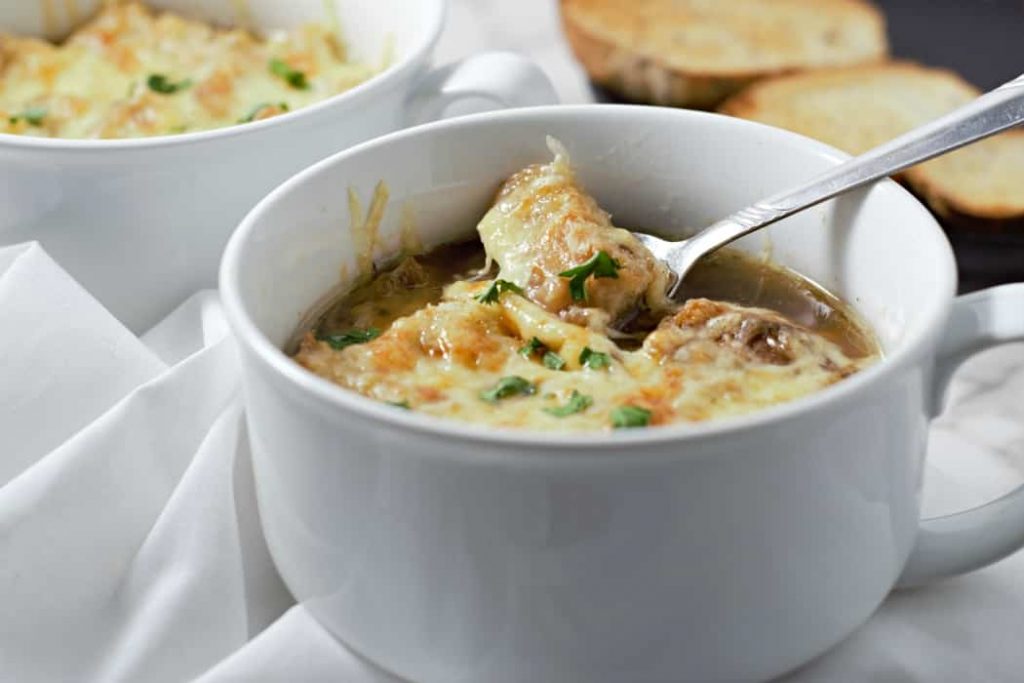 cheesy french onion soup in a white mug with green onion and melty cheese