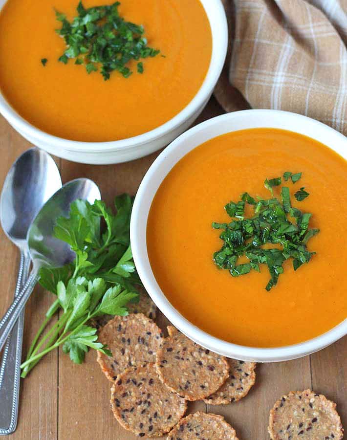 Butternut Squash Sweet Potato and Carrot Slow Cooker Soup in white bowls with parsley sprinkle spoons and crackers