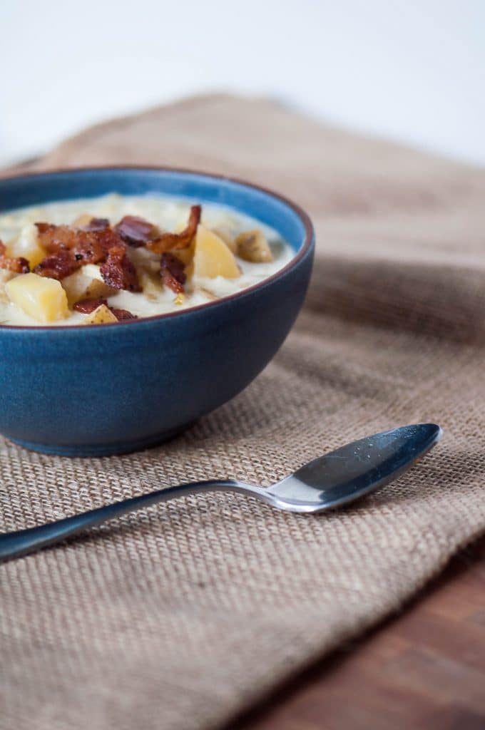 Slow cooker potato corn chowder soup in a blue bowl with bacon and a spoon