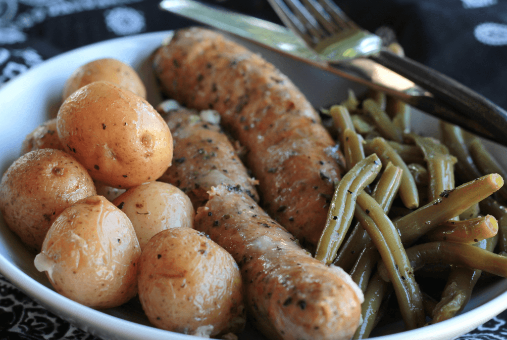 Italian sausage potatoes and green beans in a white bowl with fork and knife