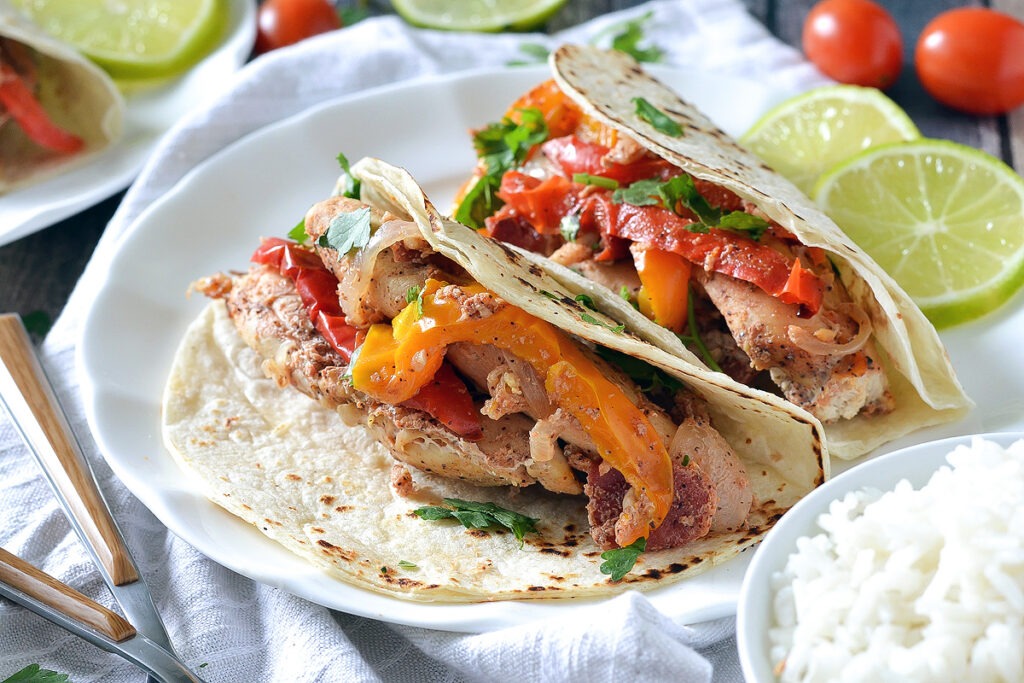 slow cooker chicken fajitas with yellow and red bell peppers in flour tortillas on a white plate